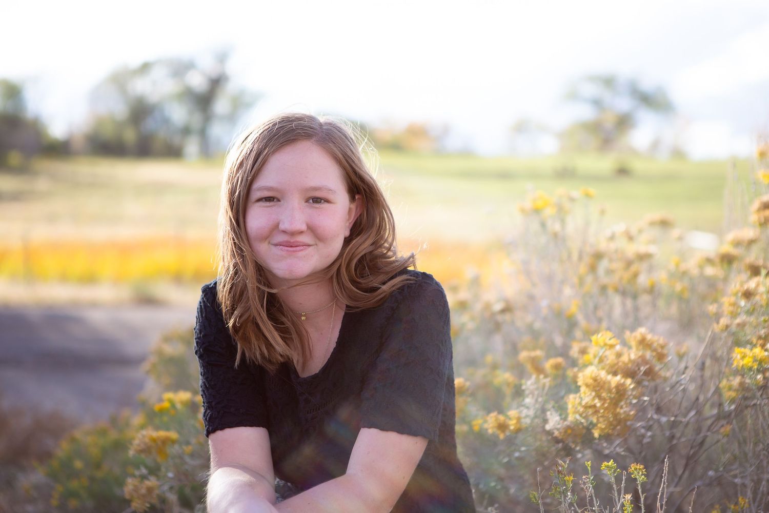 Portrait of person in black top seated outdoors with golden field in background.