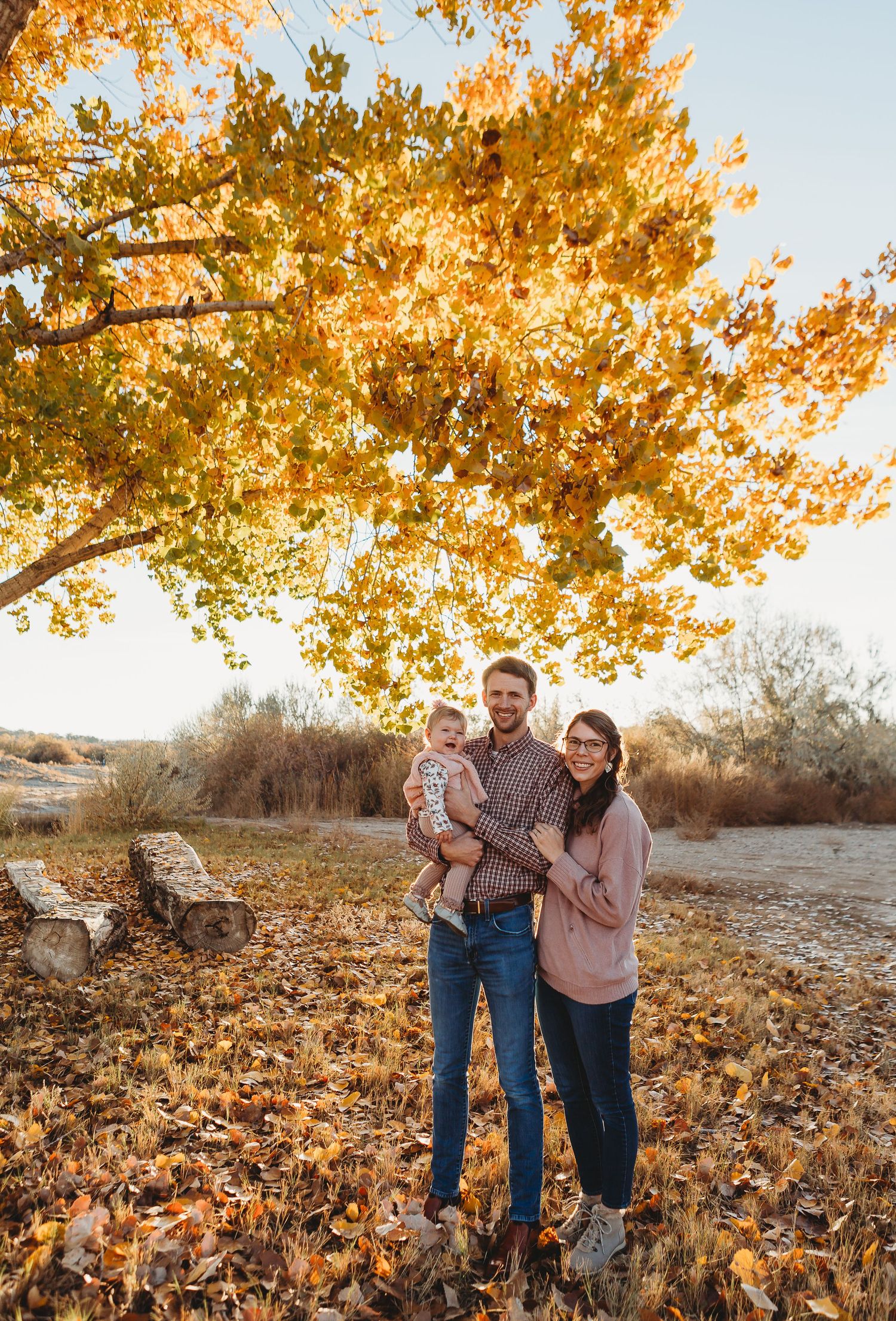 A family stands together under golden fall foliage in a scenic outdoor setting.