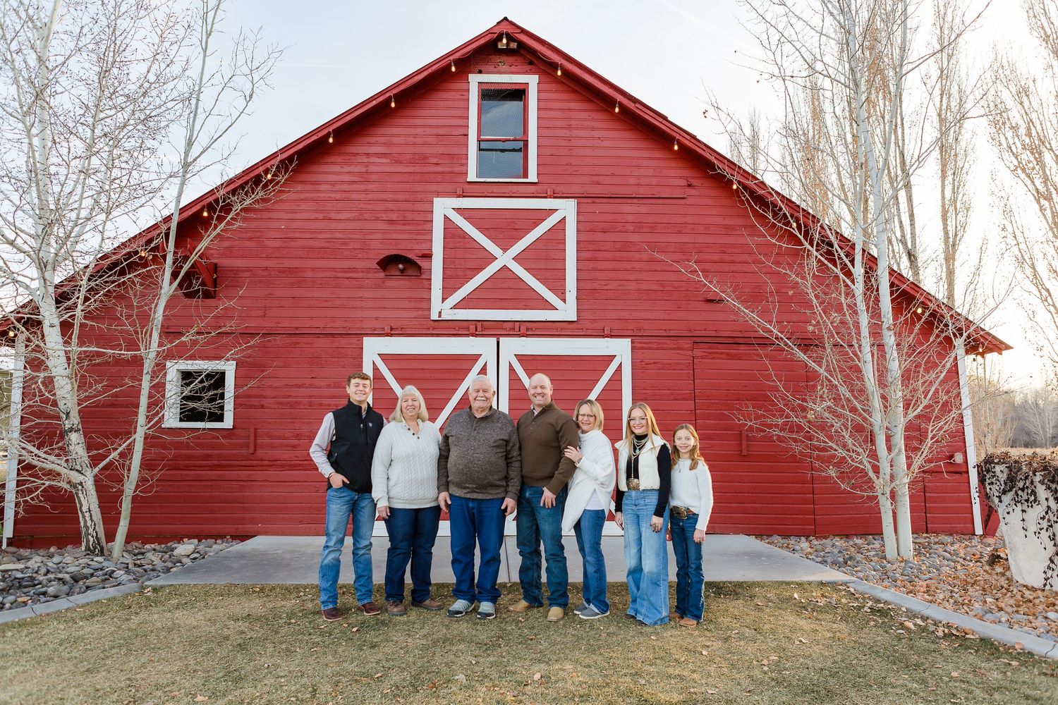 A small group poses together in front of a classic red barn with white X-shaped door designs.