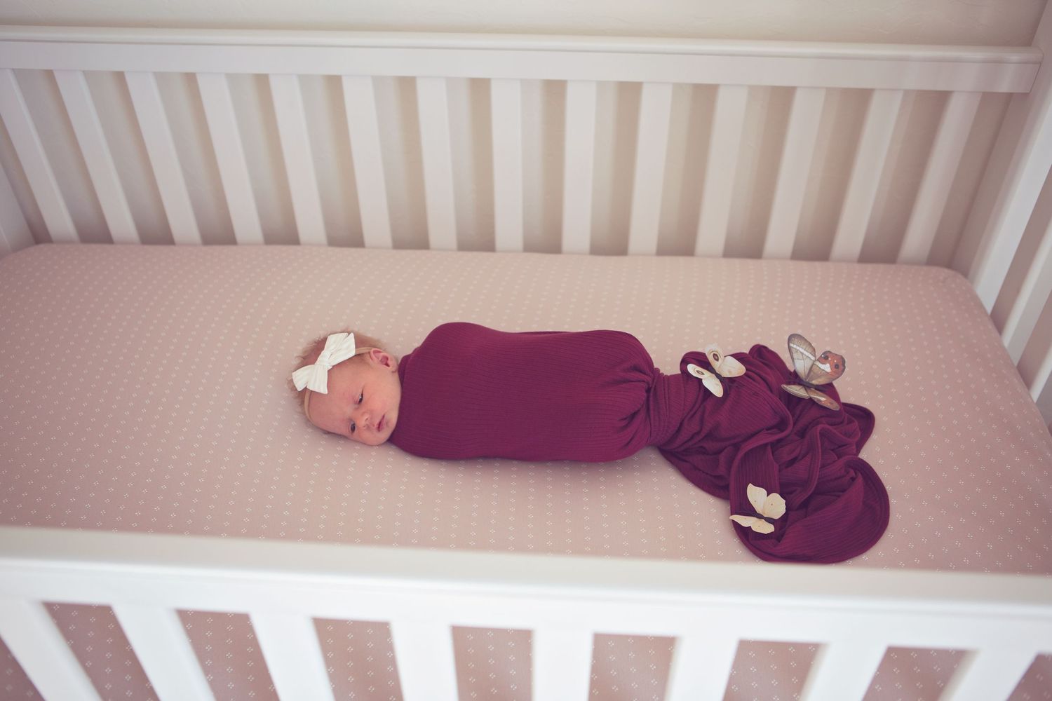 Baby in purple outfit sleeping peacefully in white crib.
