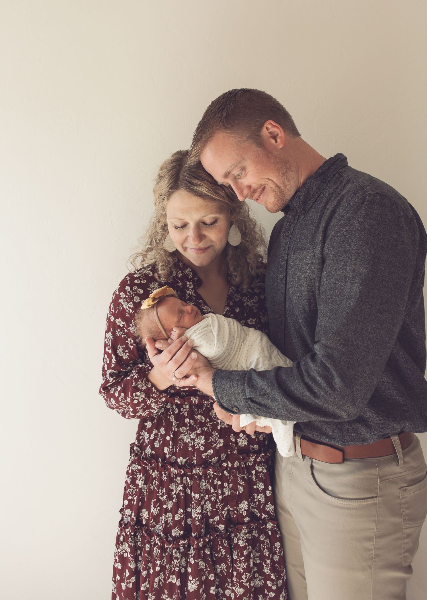 A tender family moment as parents hold their newborn baby against a neutral background.