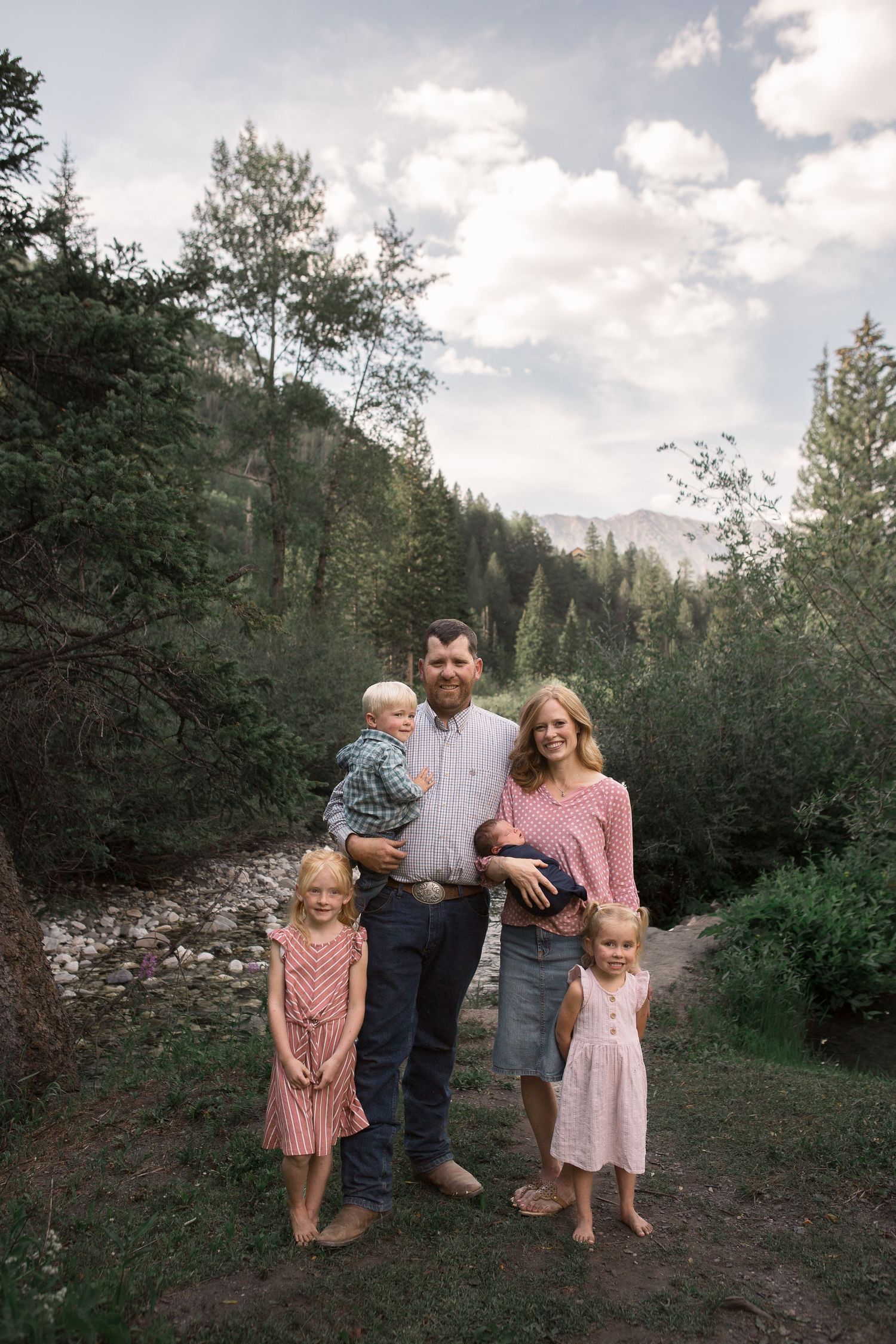 Family portrait in natural mountain setting with stream and forest backdrop.