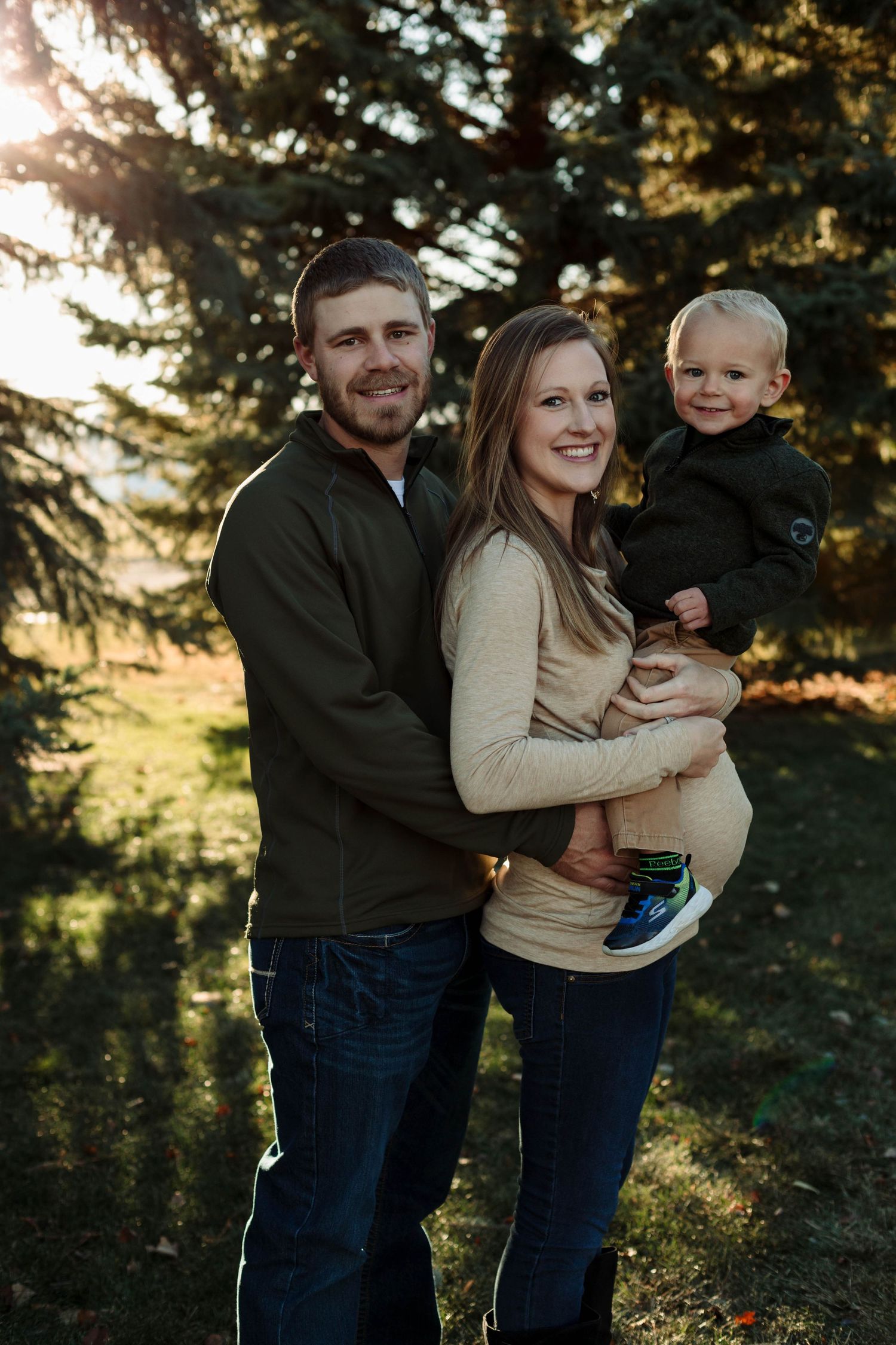 Loving family moment captured outdoors with expecting mother and father holding toddler.