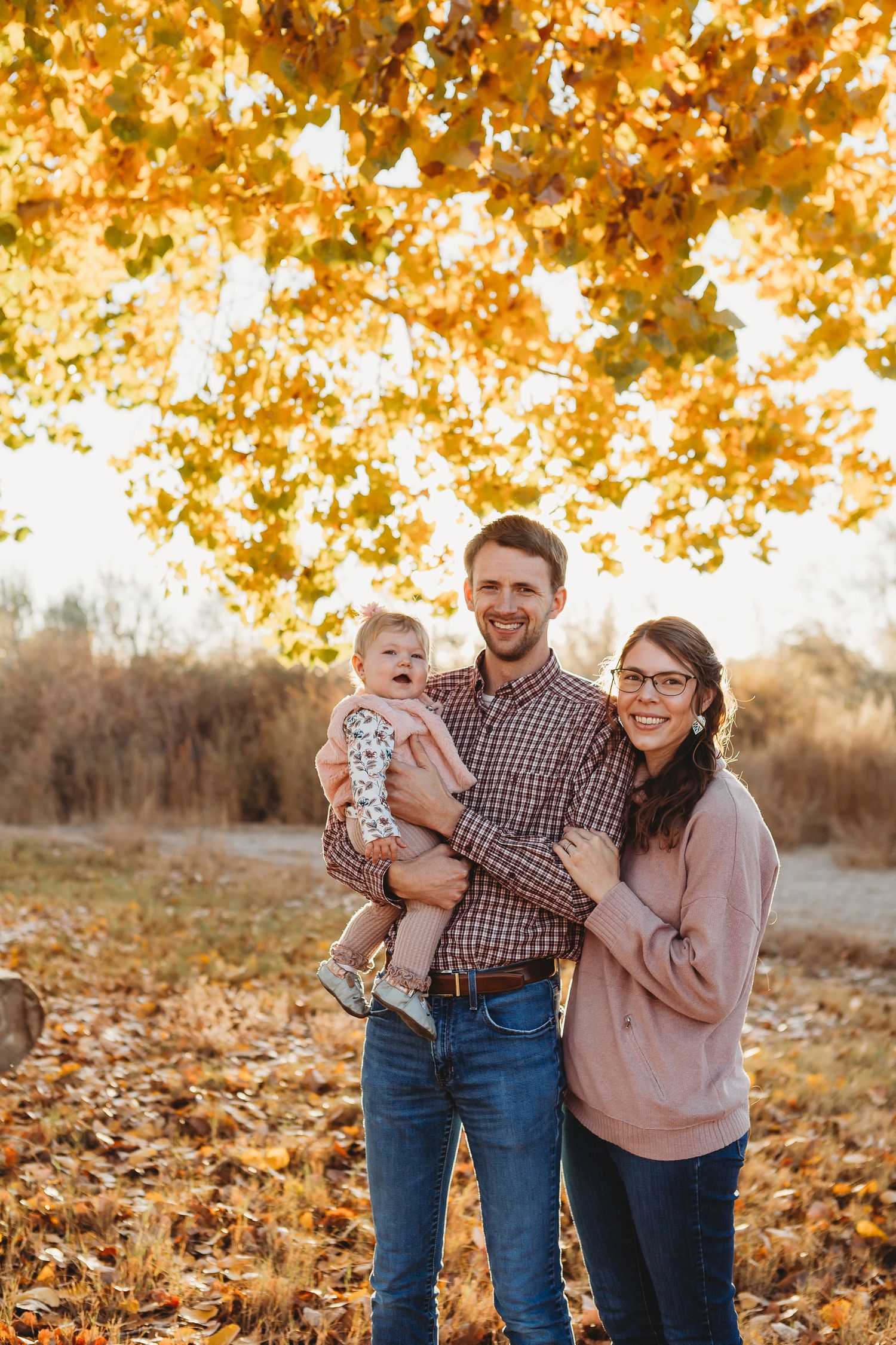 A young family smiles together during an autumn outdoor photoshoot under golden leaves.