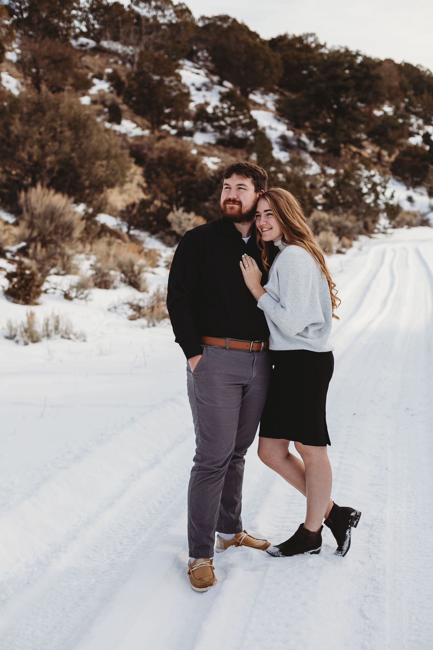 Couple sharing an intimate moment on a snow-covered path with mountains in the background.
