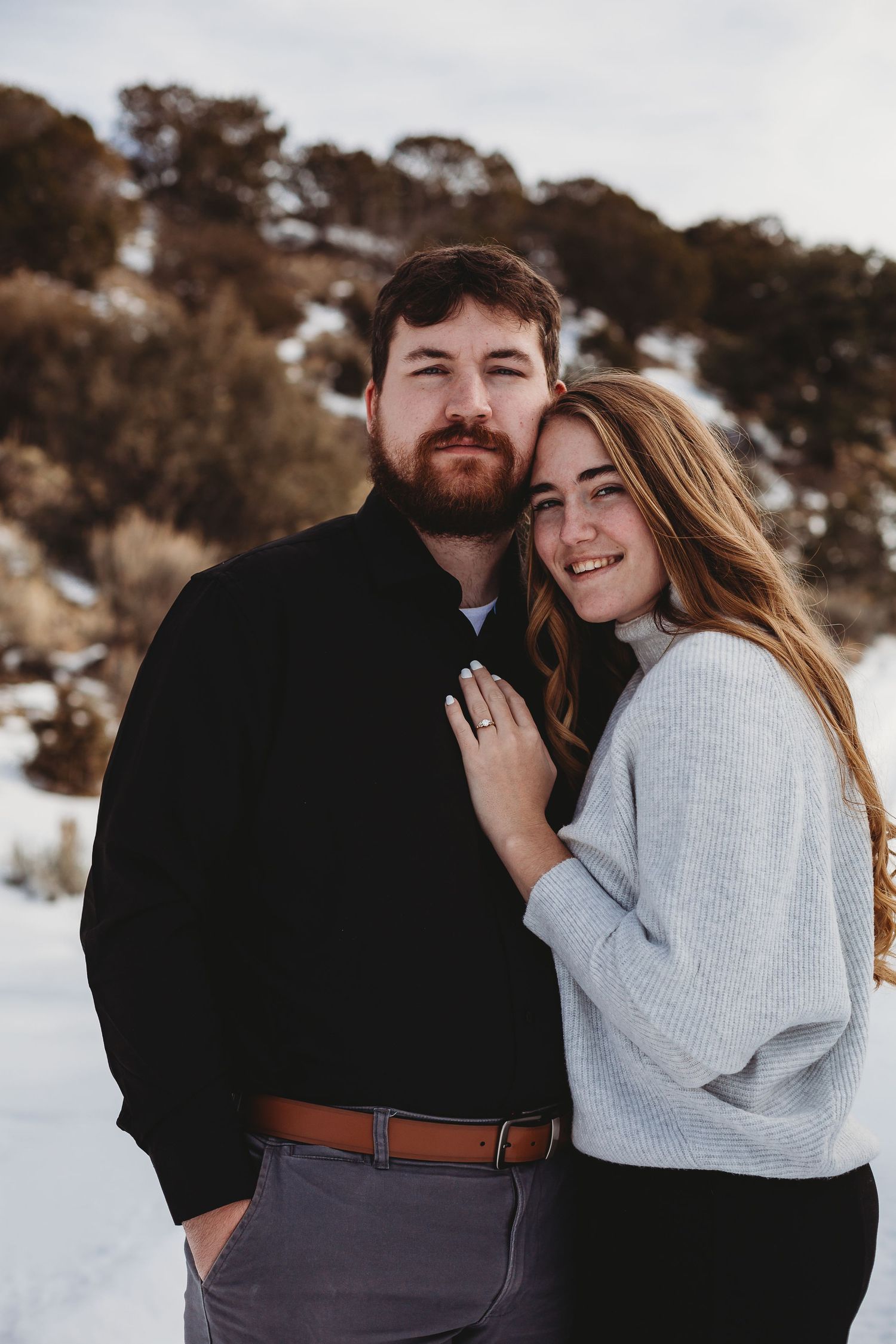 Close-up portrait of a couple in winter attire against a snowy mountainous background.