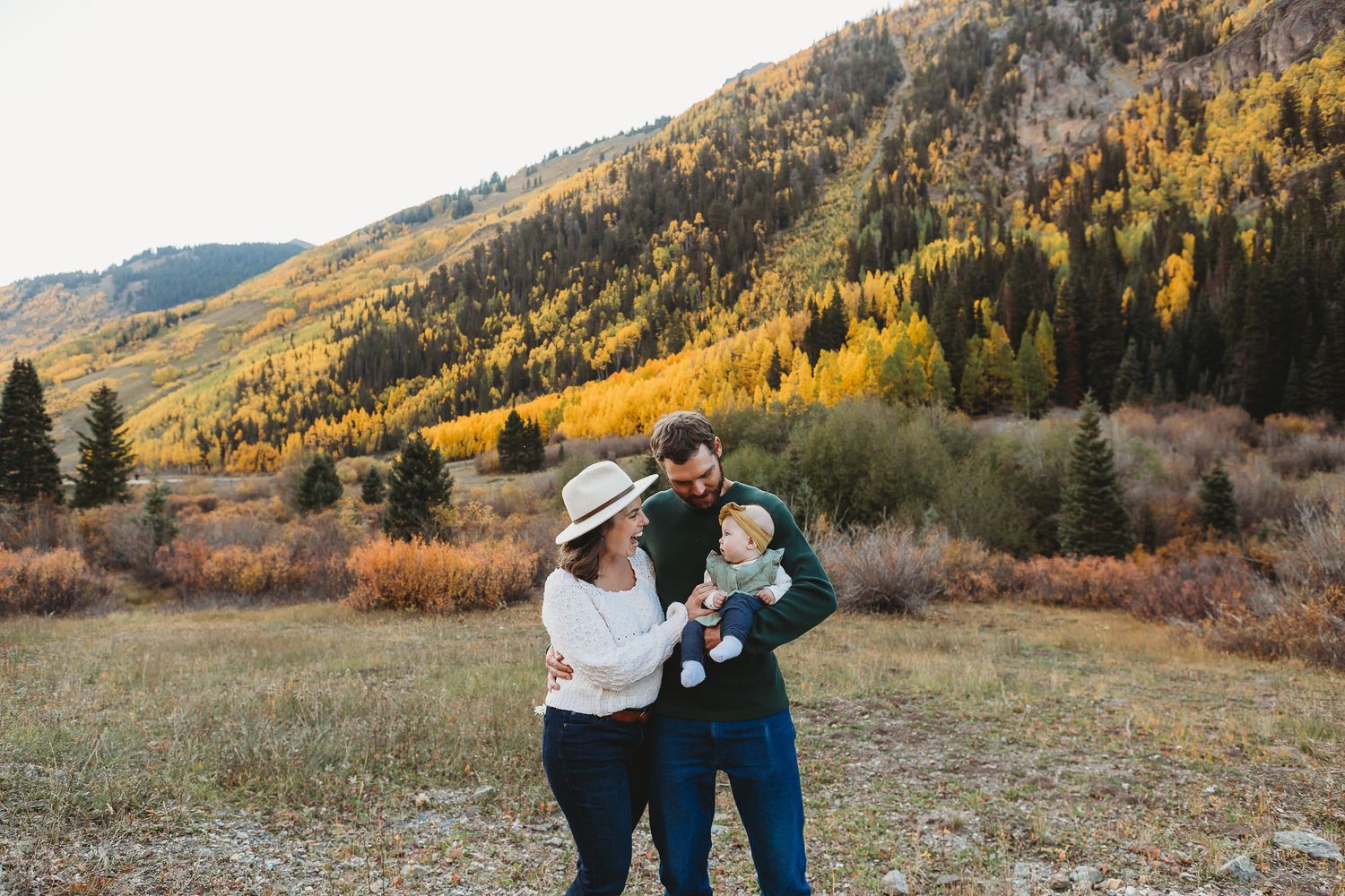 Family shares laughter in mountain meadow with autumn colors.