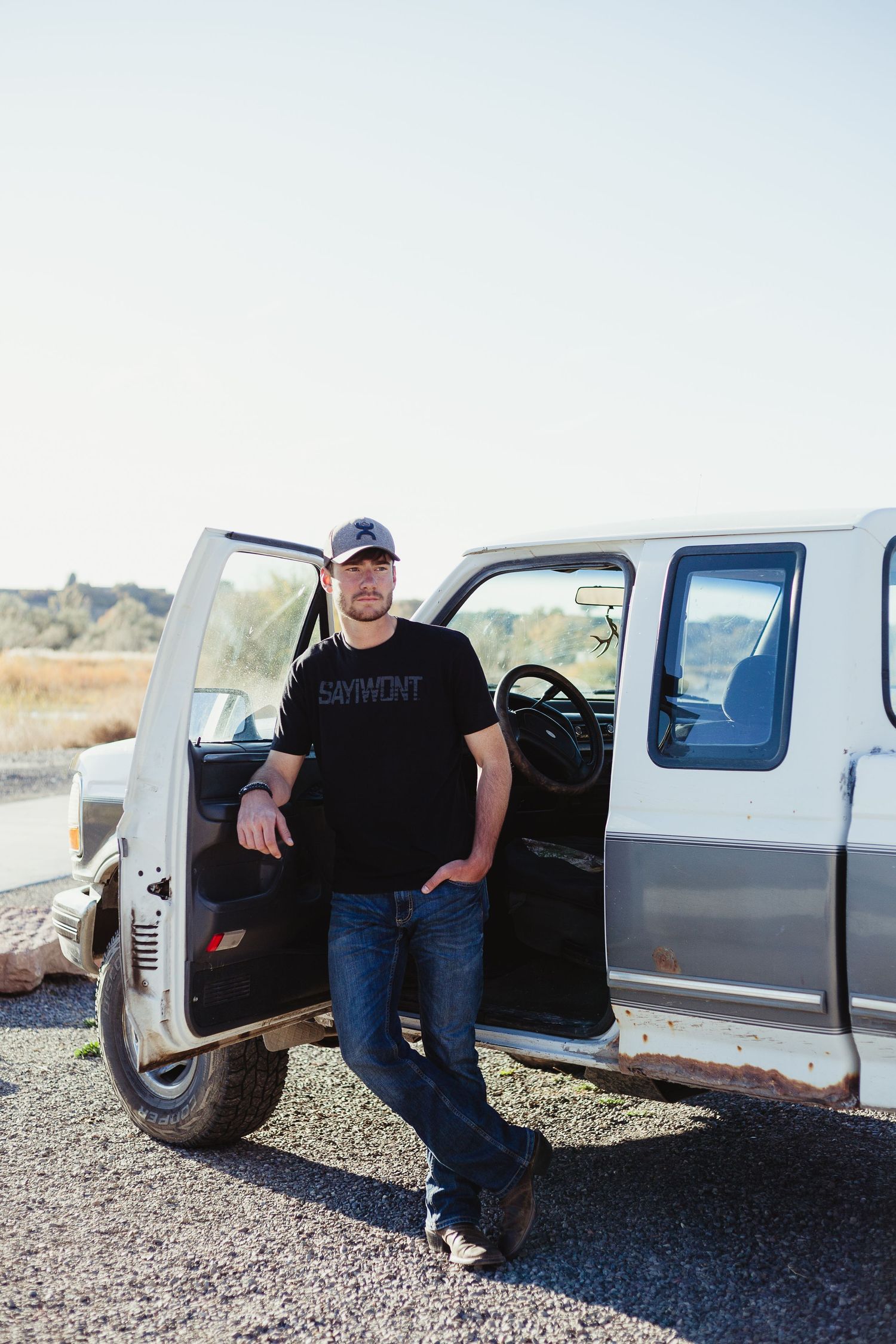 Person standing by open door of vintage white pickup truck in rural setting.