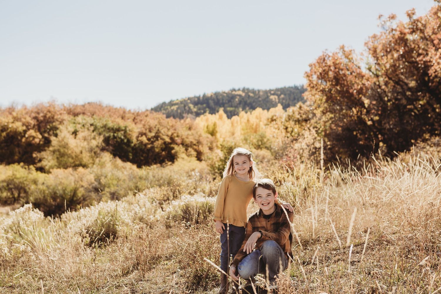Two people posing in a golden autumn field with mountain backdrop.