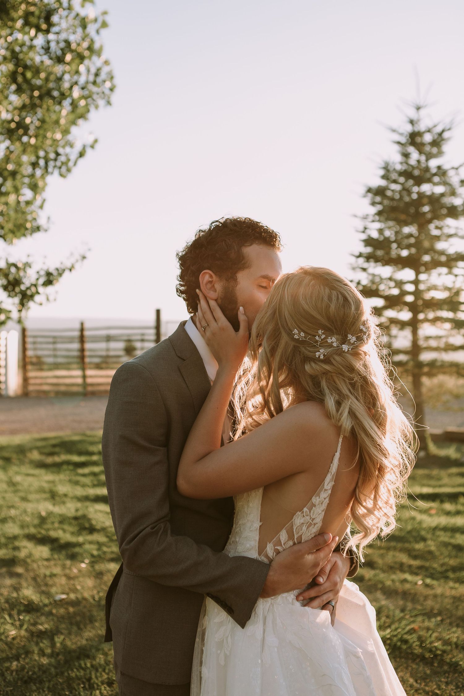 Romantic sunset wedding portrait shows newlyweds embracing in an outdoor garden setting with evergreen trees.