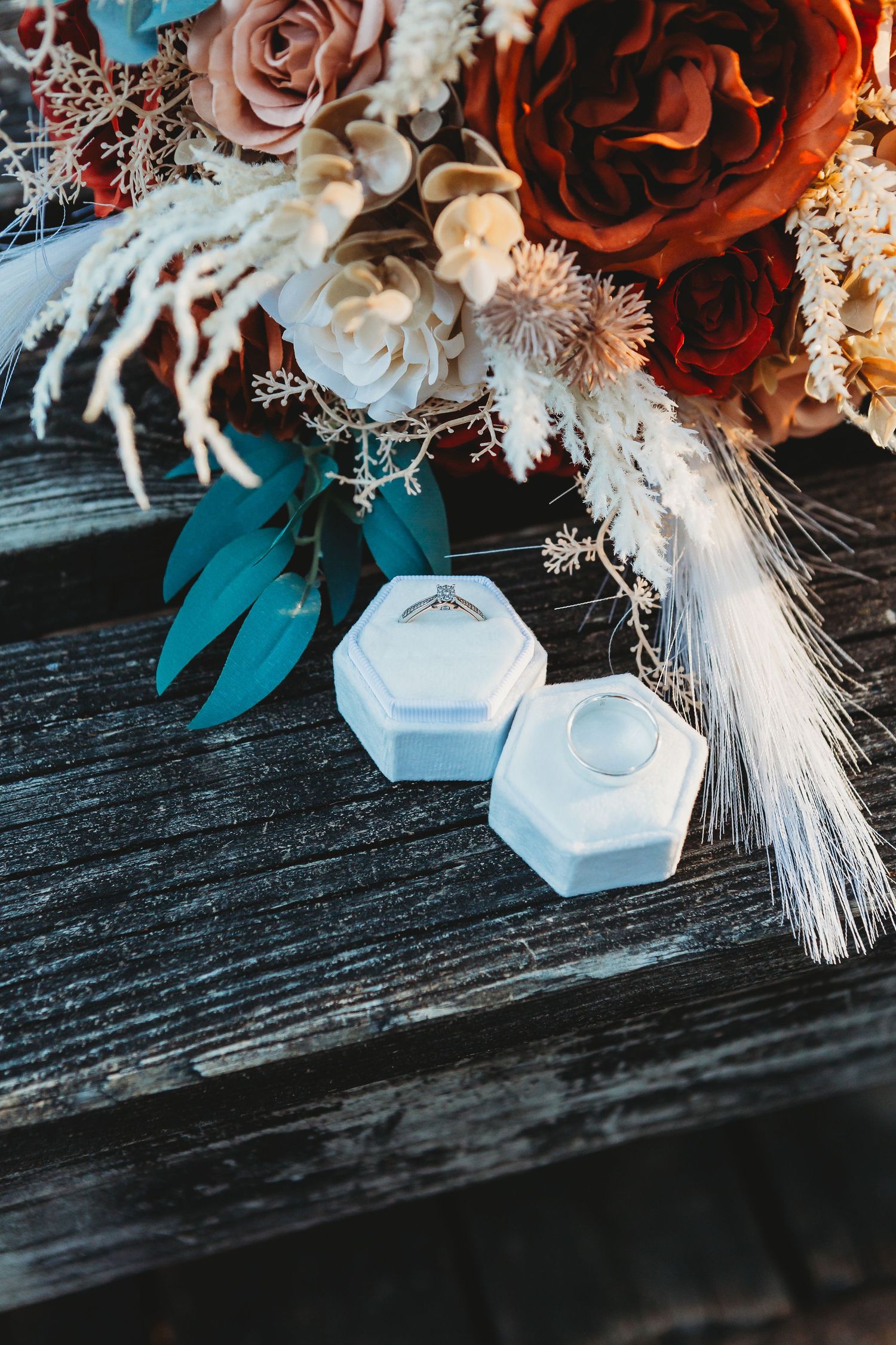 Wedding rings in hexagonal boxes displayed with dramatic floral arrangement.