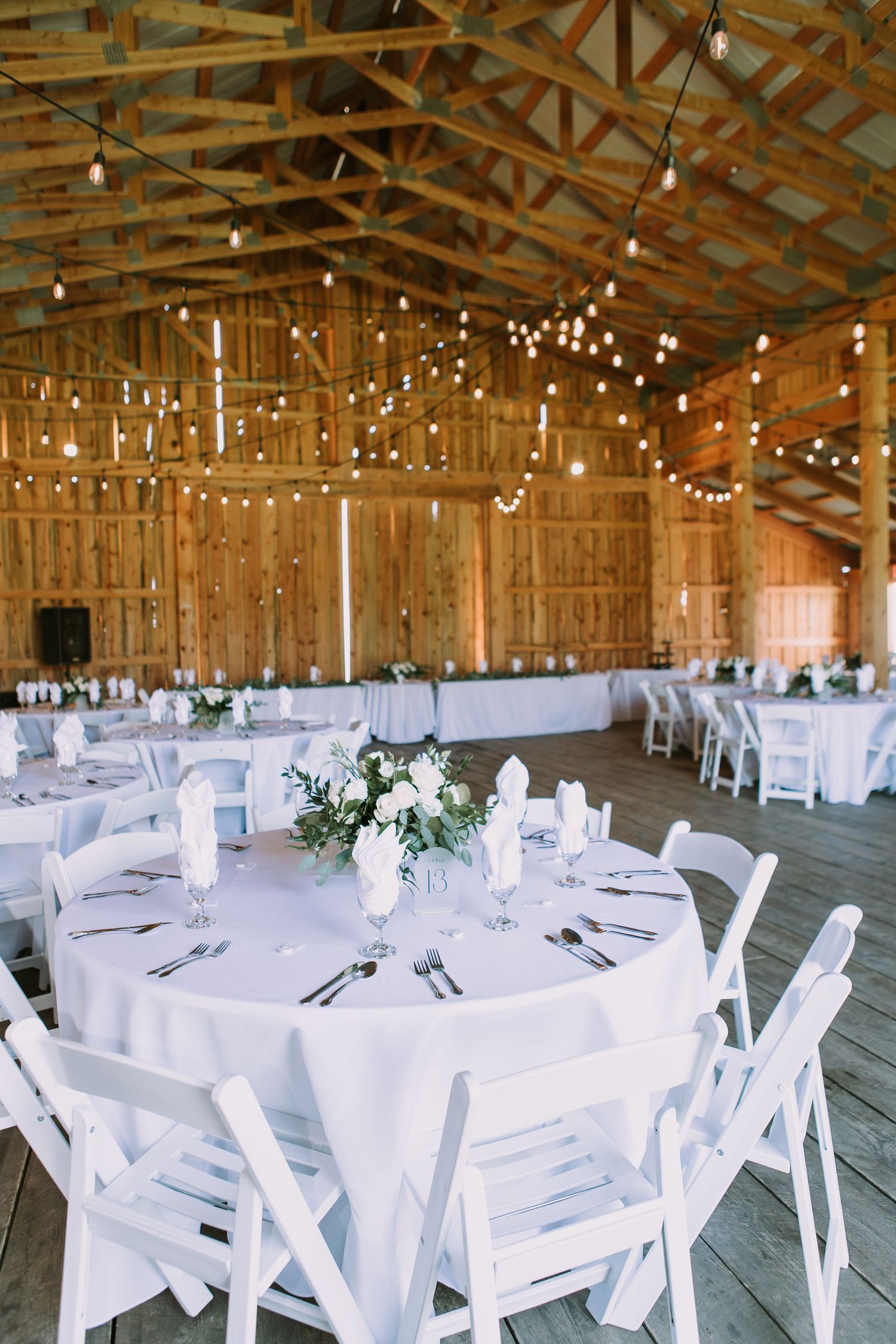 Barn reception hall with string lights, white round tables, and elegant table settings.