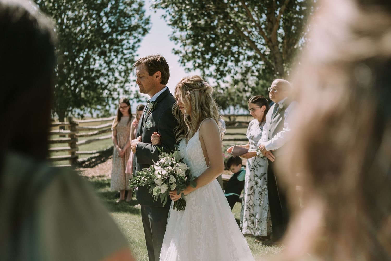 Intimate outdoor wedding ceremony with guests watching couple exchange vows under trees.