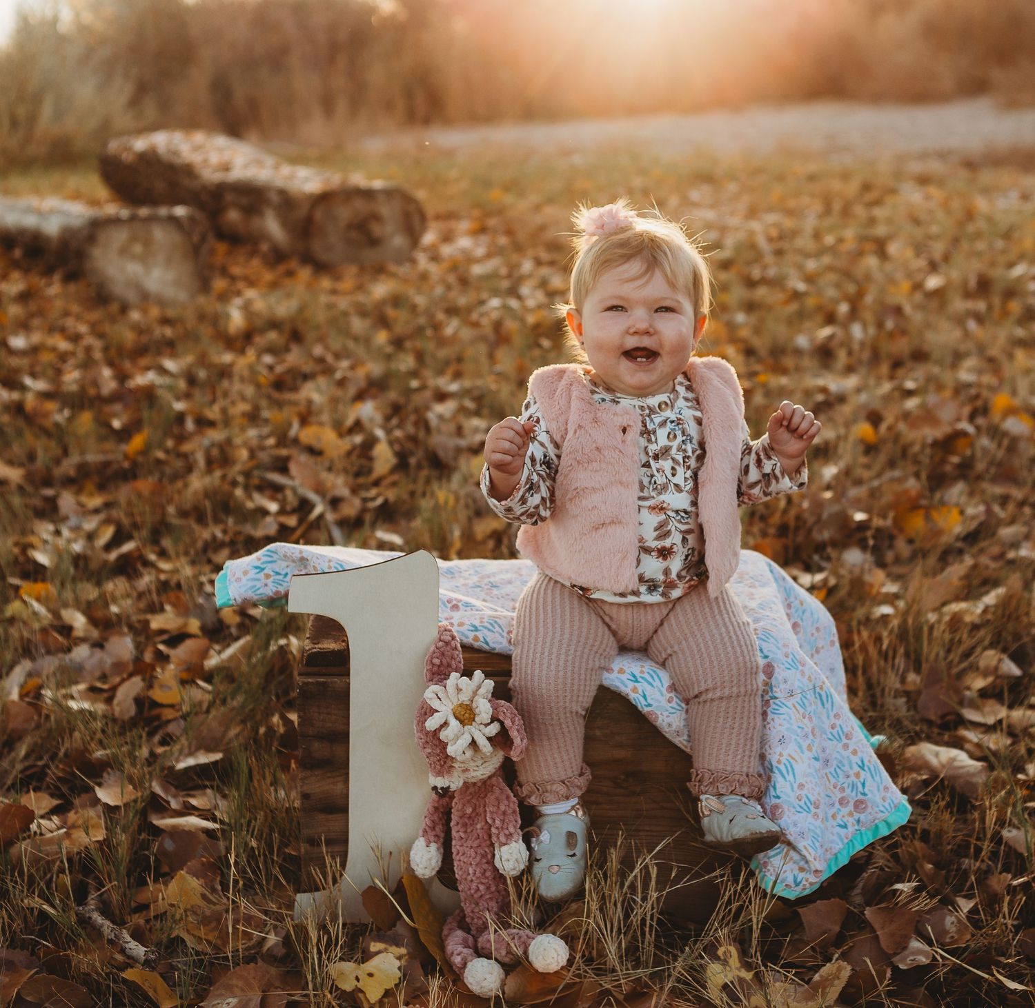 Happy toddler sitting on decorative number one prop with a stuffed bunny and blanket in fall setting.