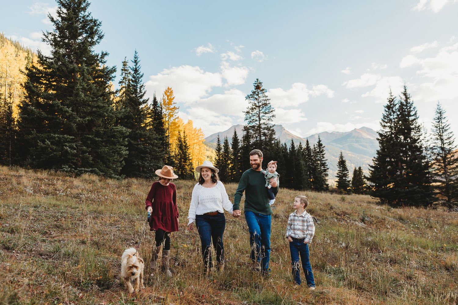 People and their dog enjoy an autumn hike on a mountain trail with vibrant yellow aspen trees.