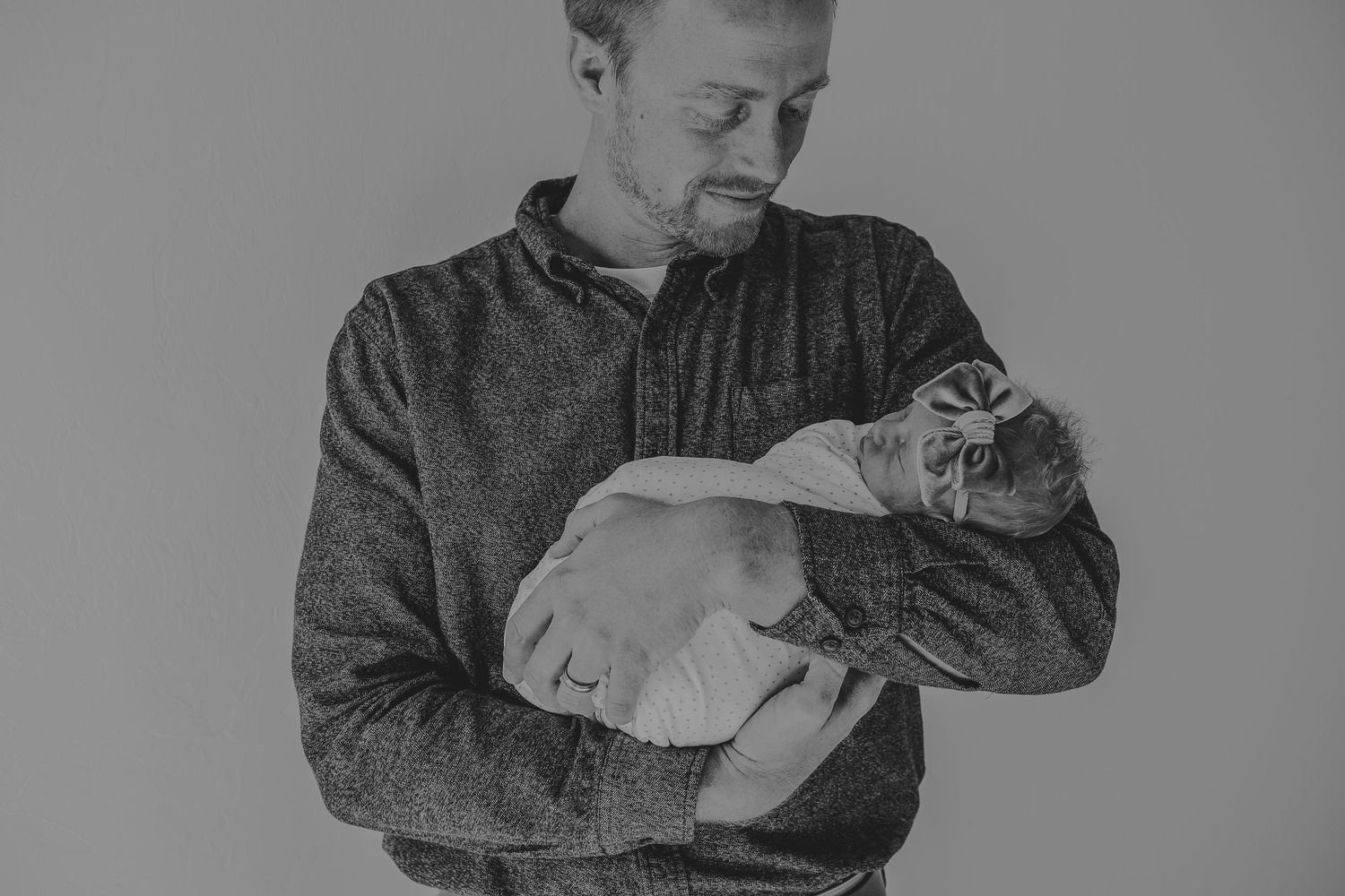 Black and white image of person in grey sweater tenderly holding a swaddled infant.