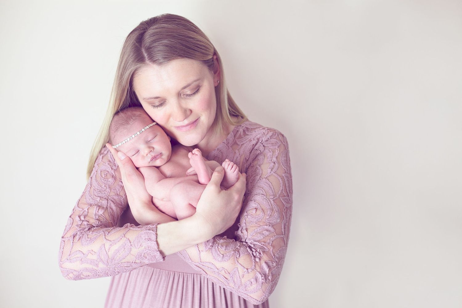 A tender moment between mother and newborn baby in soft pink tones.