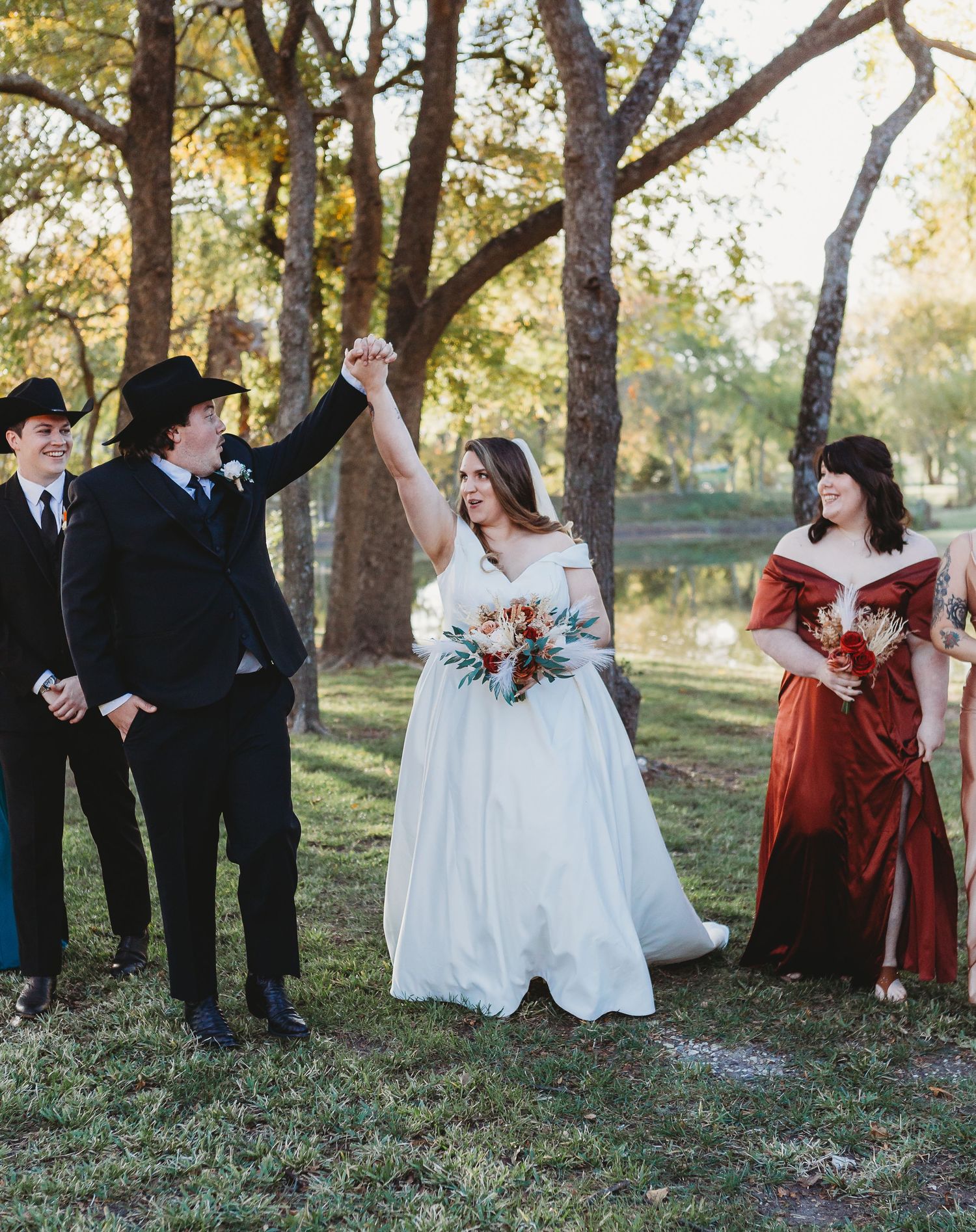 Wedding party celebrates with raised hands during outdoor autumn ceremony.