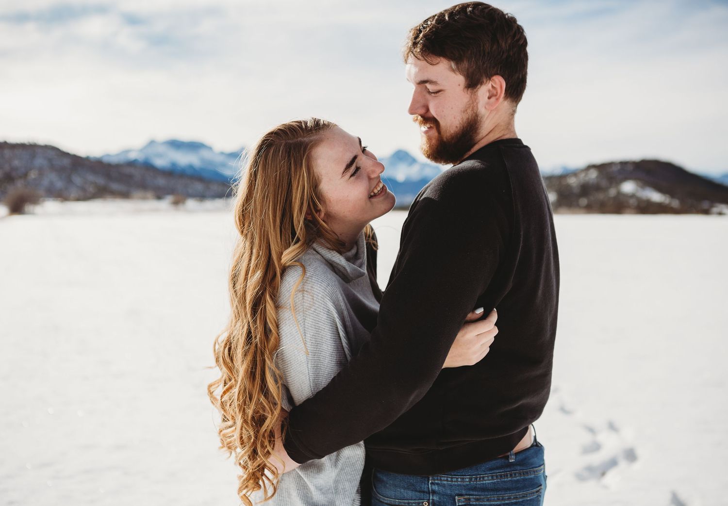 A romantic winter engagement photoshoot against a snowy mountain backdrop.