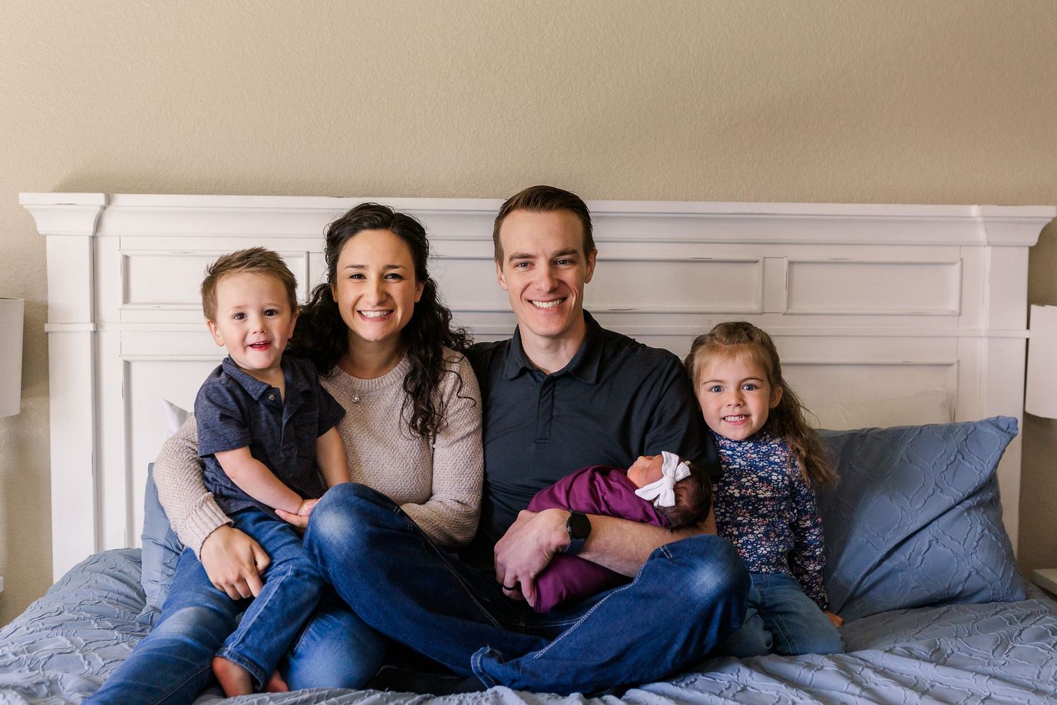 Happy family with children posing together on bed with white headboard.