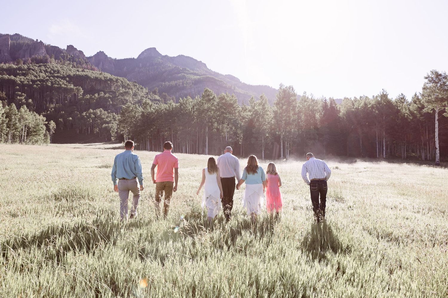 Family silhouettes walking together through golden mountain meadow at sunset.