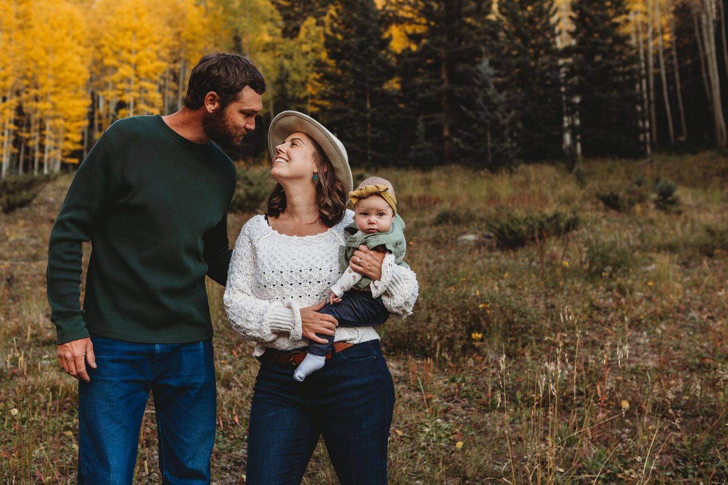 Sweet family portrait in autumn field with golden aspen trees in background.