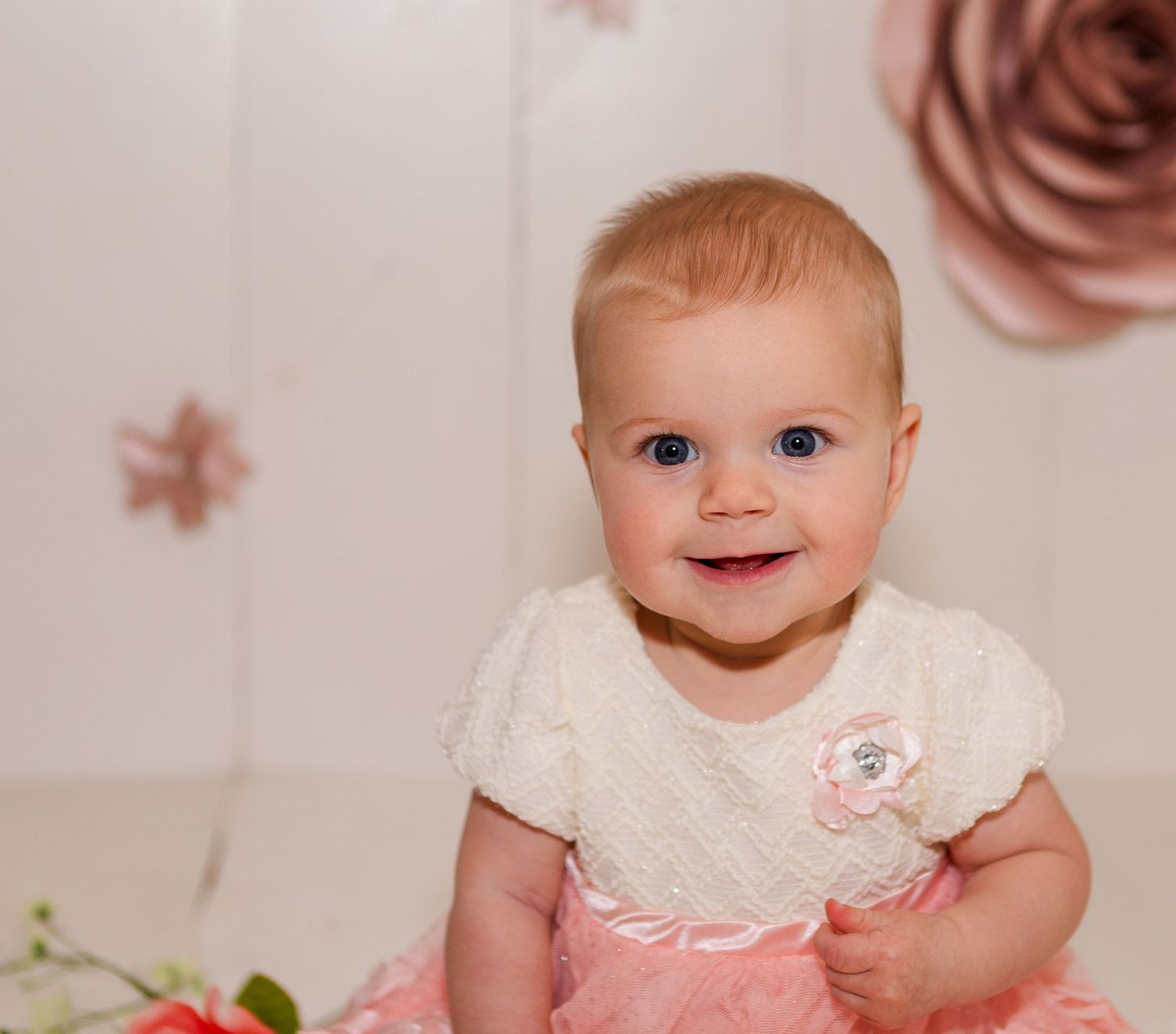Baby dressed in pink and white outfit against floral backdrop.