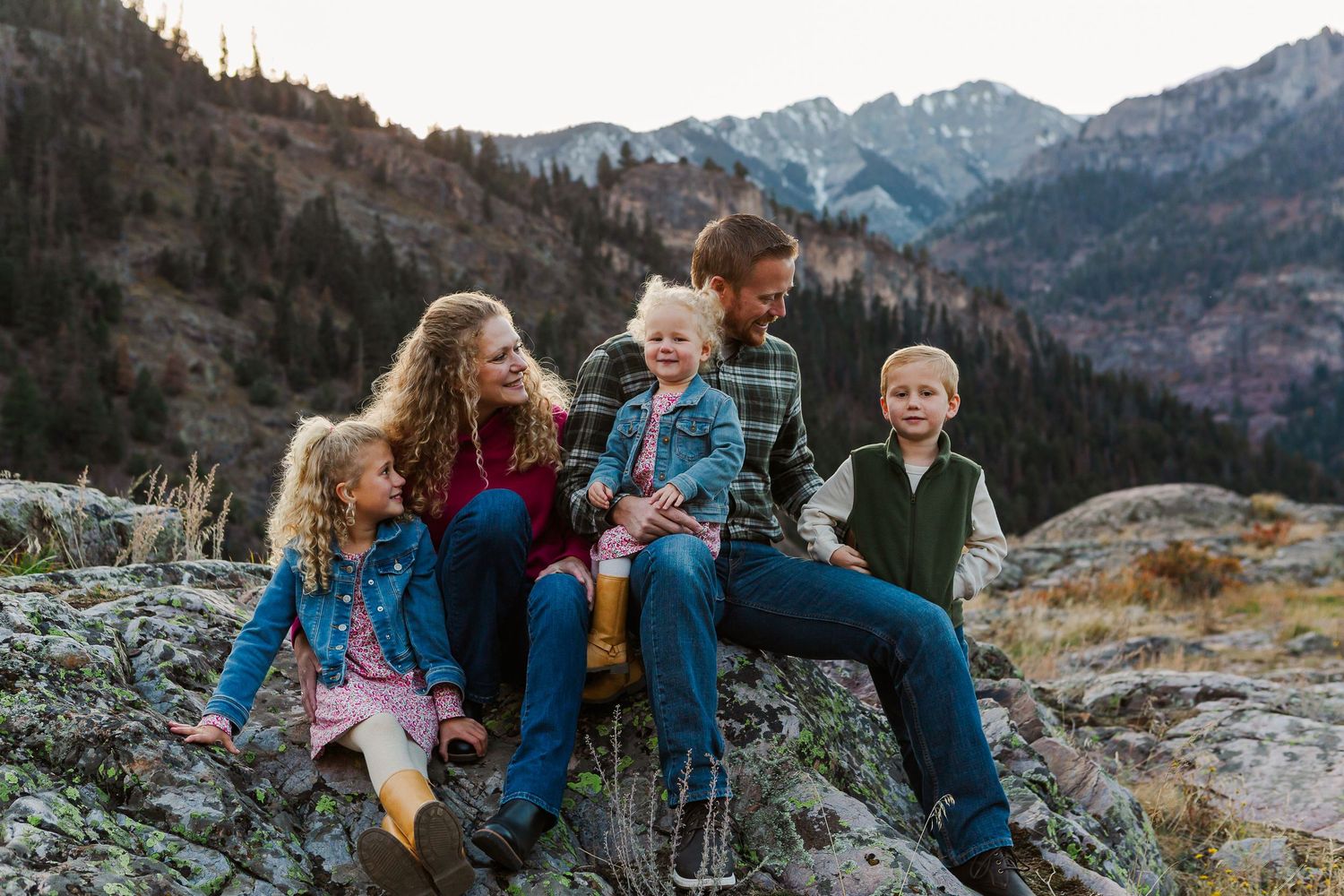 Family sitting together on rocky mountain overlook during autumn sunset with scenic mountain views.