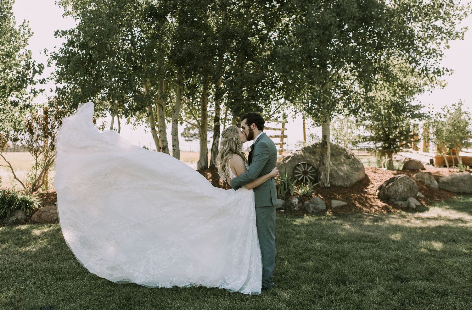 A joyful wedding photo showing the bride's dress catching the wind in a natural setting.