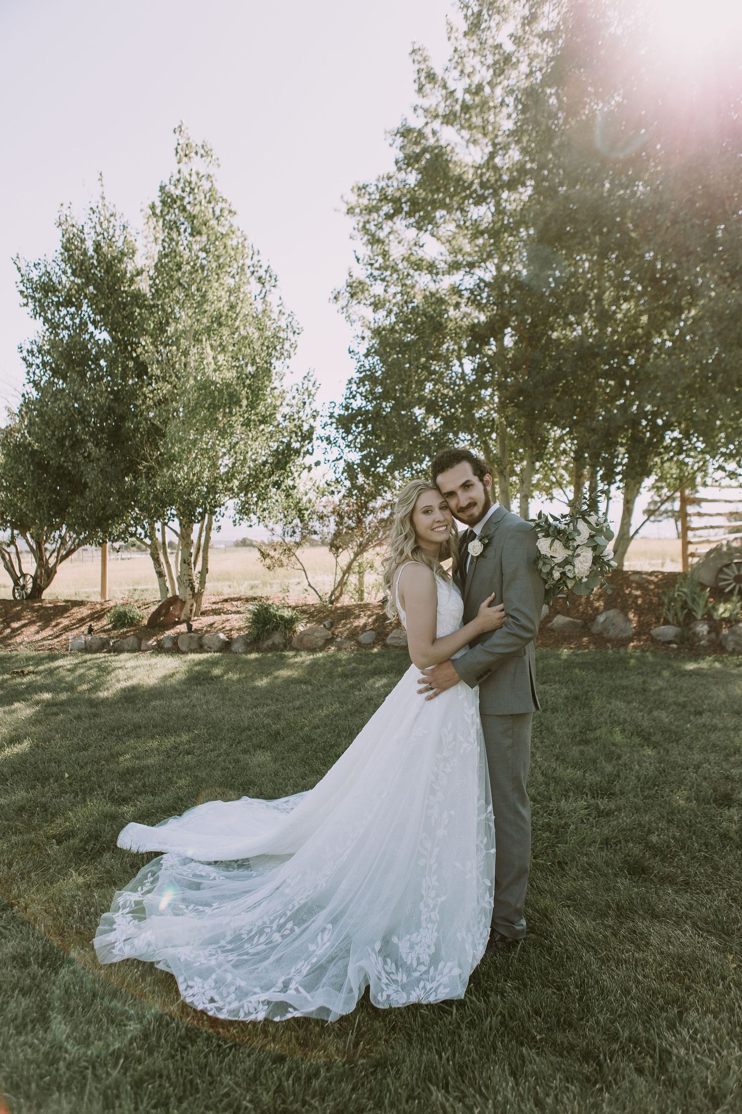 Wedding couple embraces in an outdoor garden setting with a beautifully detailed lace gown.