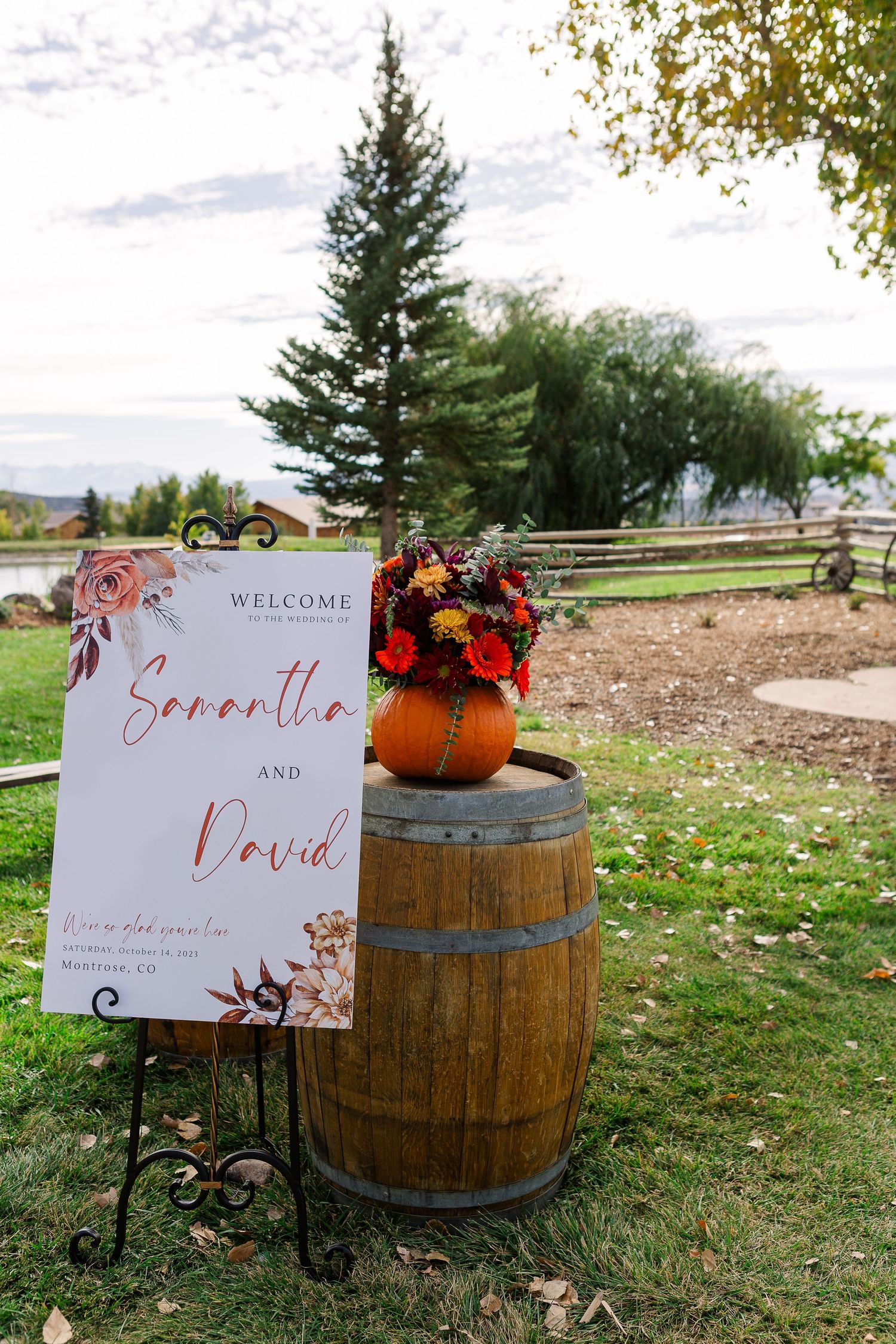 Rustic wedding welcome sign displayed on wooden barrel with fall floral arrangement and pumpkin.