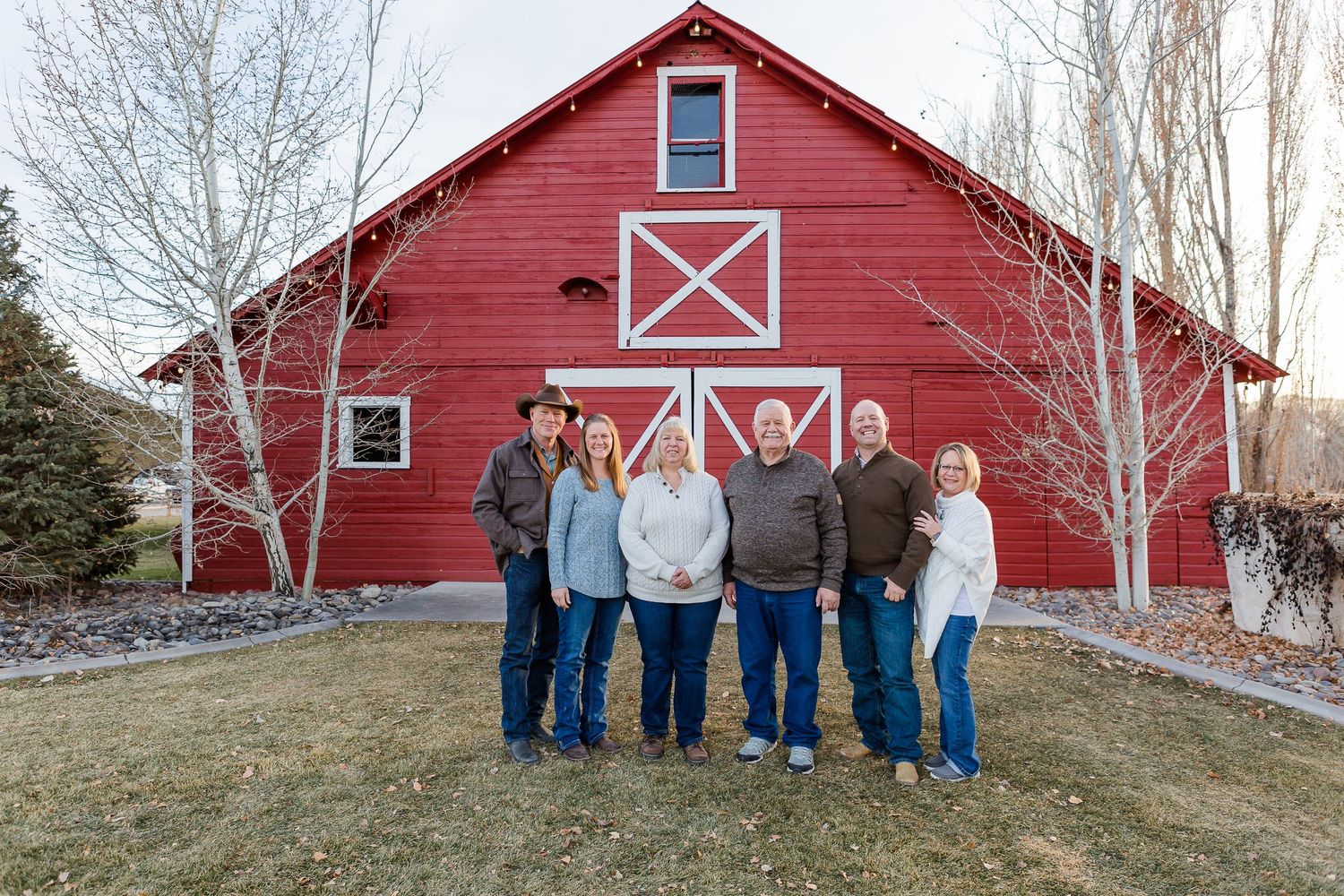 A group of people pose for a photo in front of a bright red barn with white X-pattern doors.