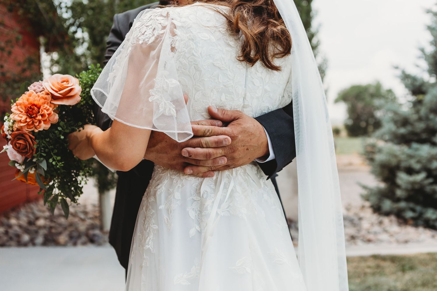 Intimate moment captured showing details of lace dress and orange rose bouquet.