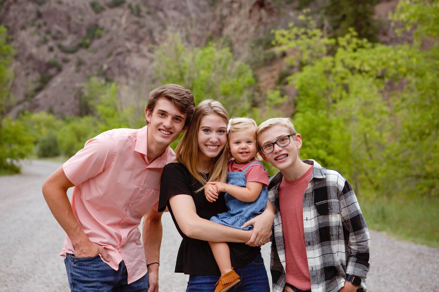 A happy family portrait taken outdoors with mountains and green foliage in the background.