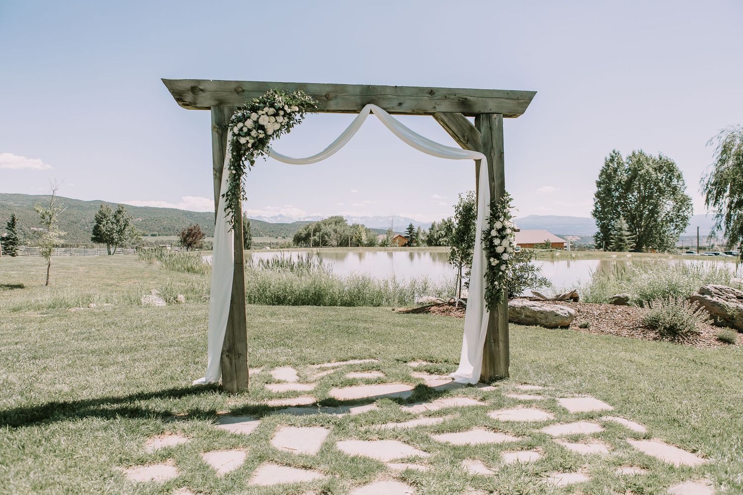 Wedding ceremony arch with flowing white fabric and stone pathway in a scenic mountain setting.