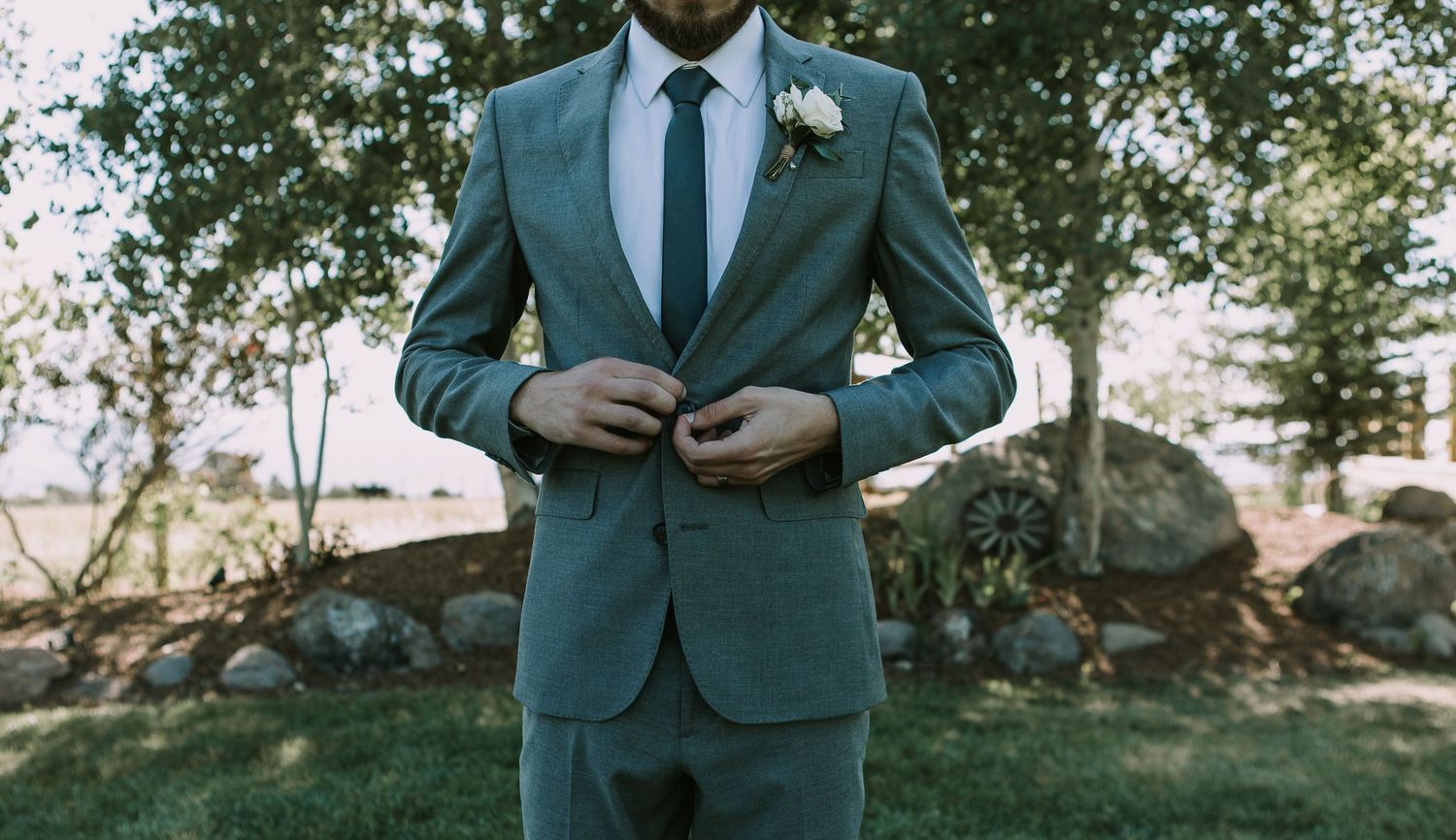 Detail shot of groom adjusting teal suit jacket outdoors.