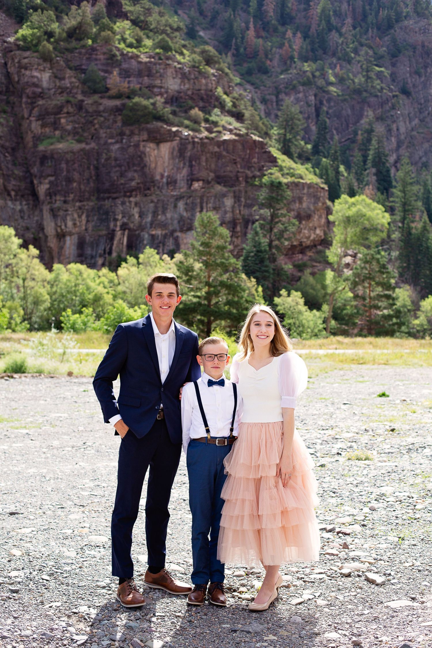 Three people in coordinated formal attire pose in front of rocky canyon landscape.