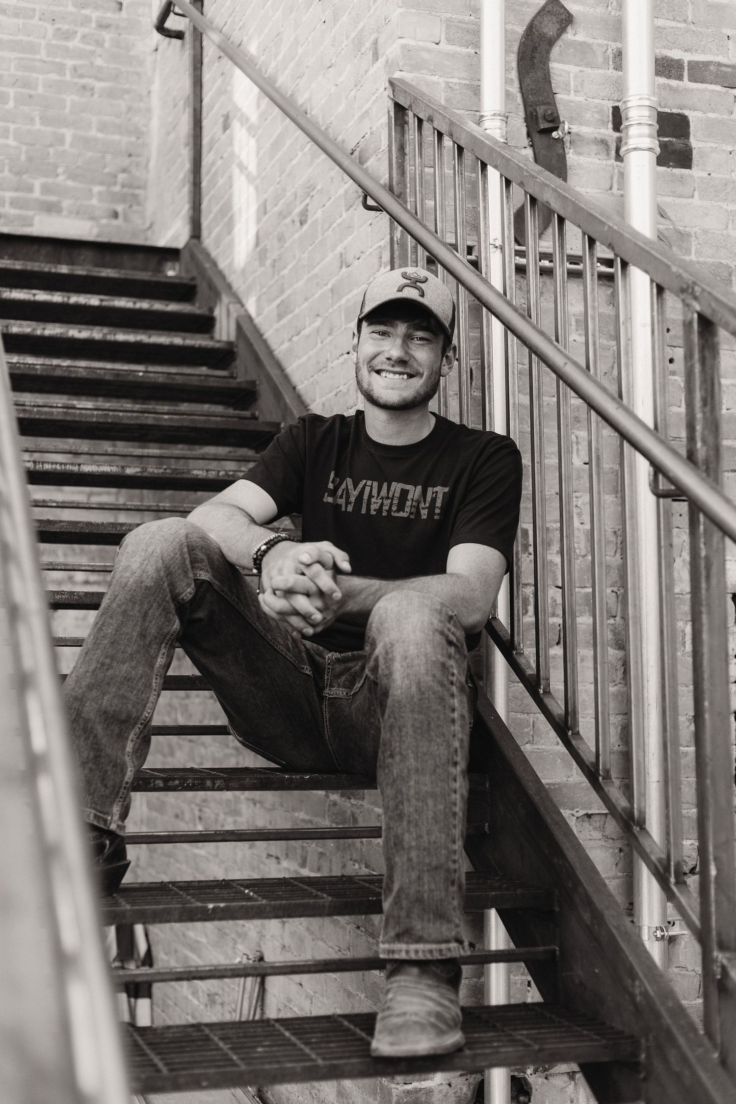 Person sitting on metal staircase wearing casual attire in black and white photo.