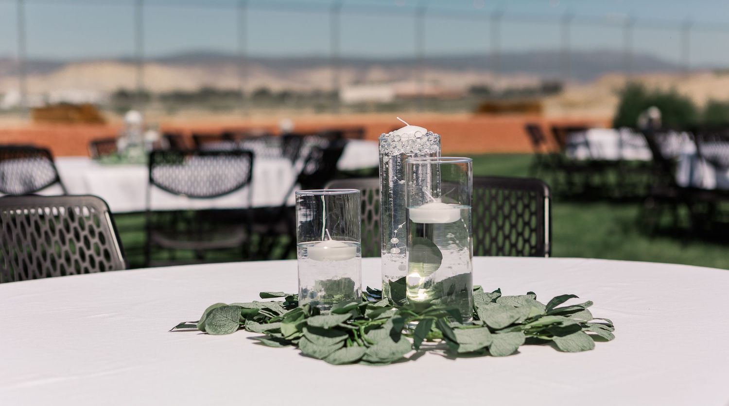 Wedding reception table centerpiece with greenery and glass candle holders.