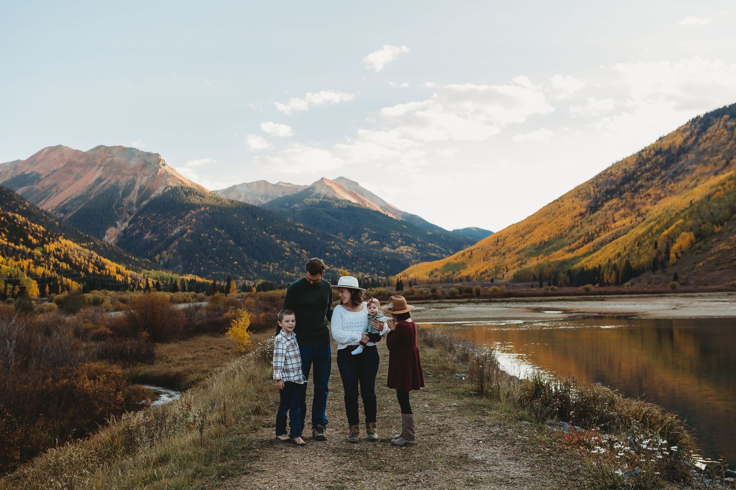Silhouette of a family walking along a mountain lake trail during golden hour.