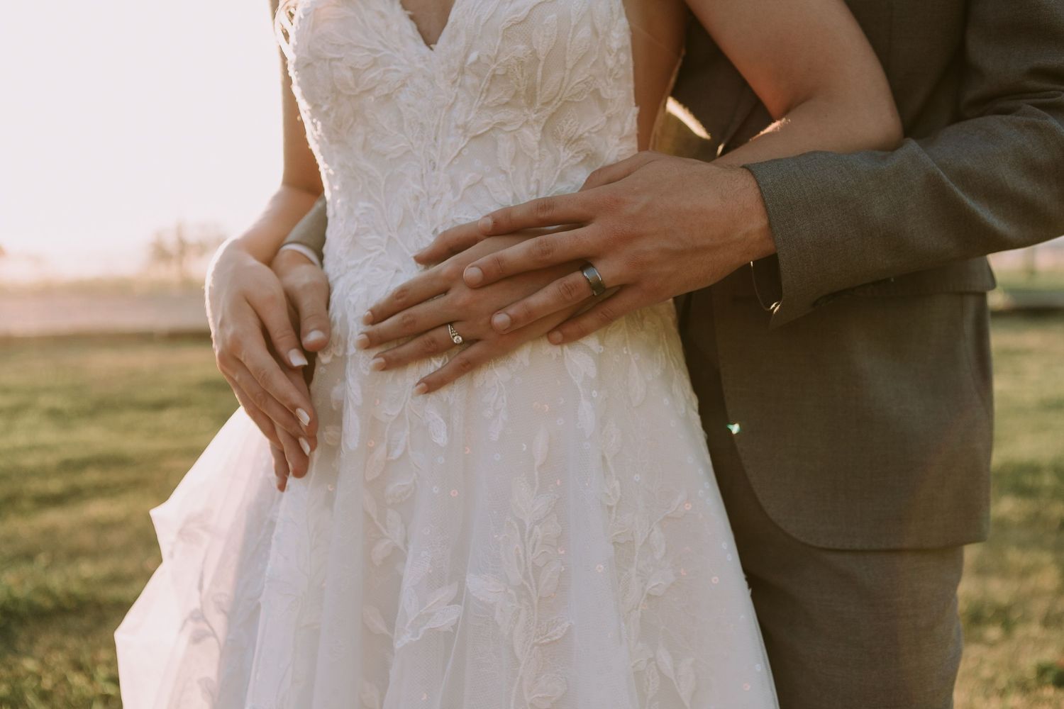 Close-up of bride in lace dress with groom's hands around her waist.