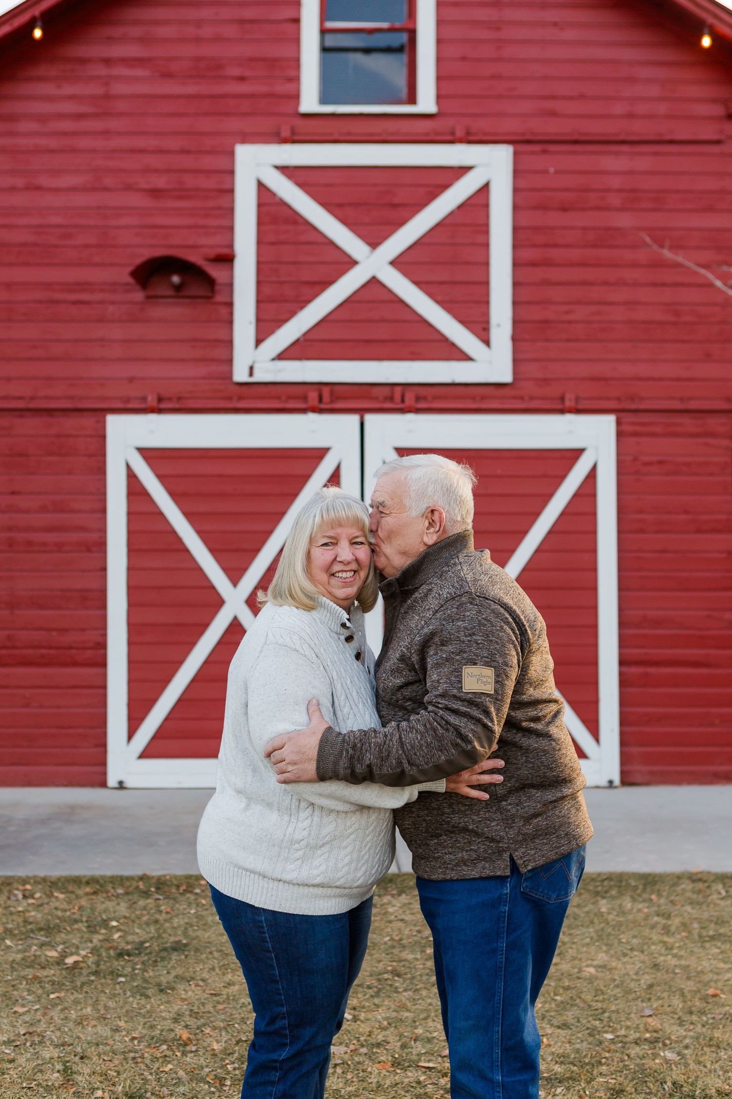 Couple sharing a tender moment while hugging in front of a red barn with white trim details.