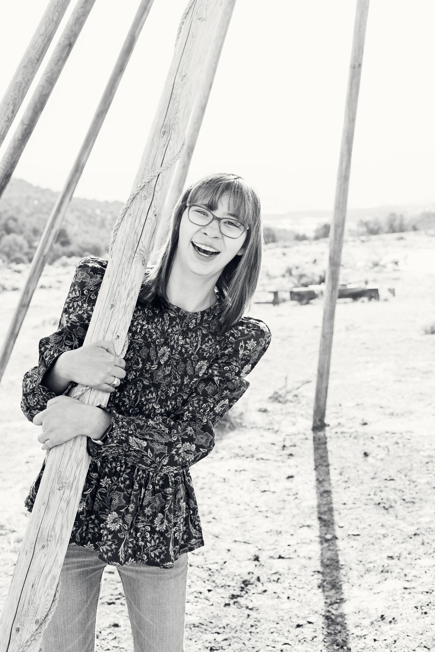 Black and white portrait of person hugging wooden pole while smiling outdoors.