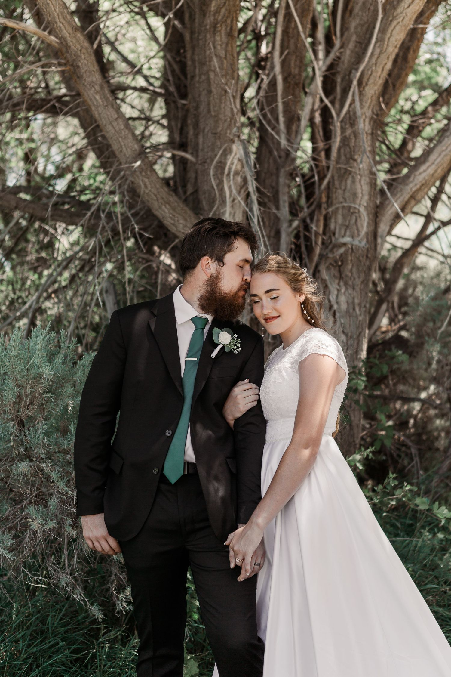 A tender wedding portrait beneath a large tree with natural greenery.