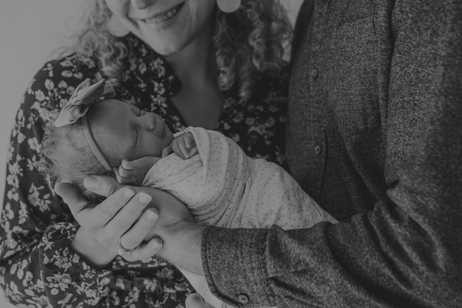 A black and white portrait of parents sharing an intimate moment with their newborn.