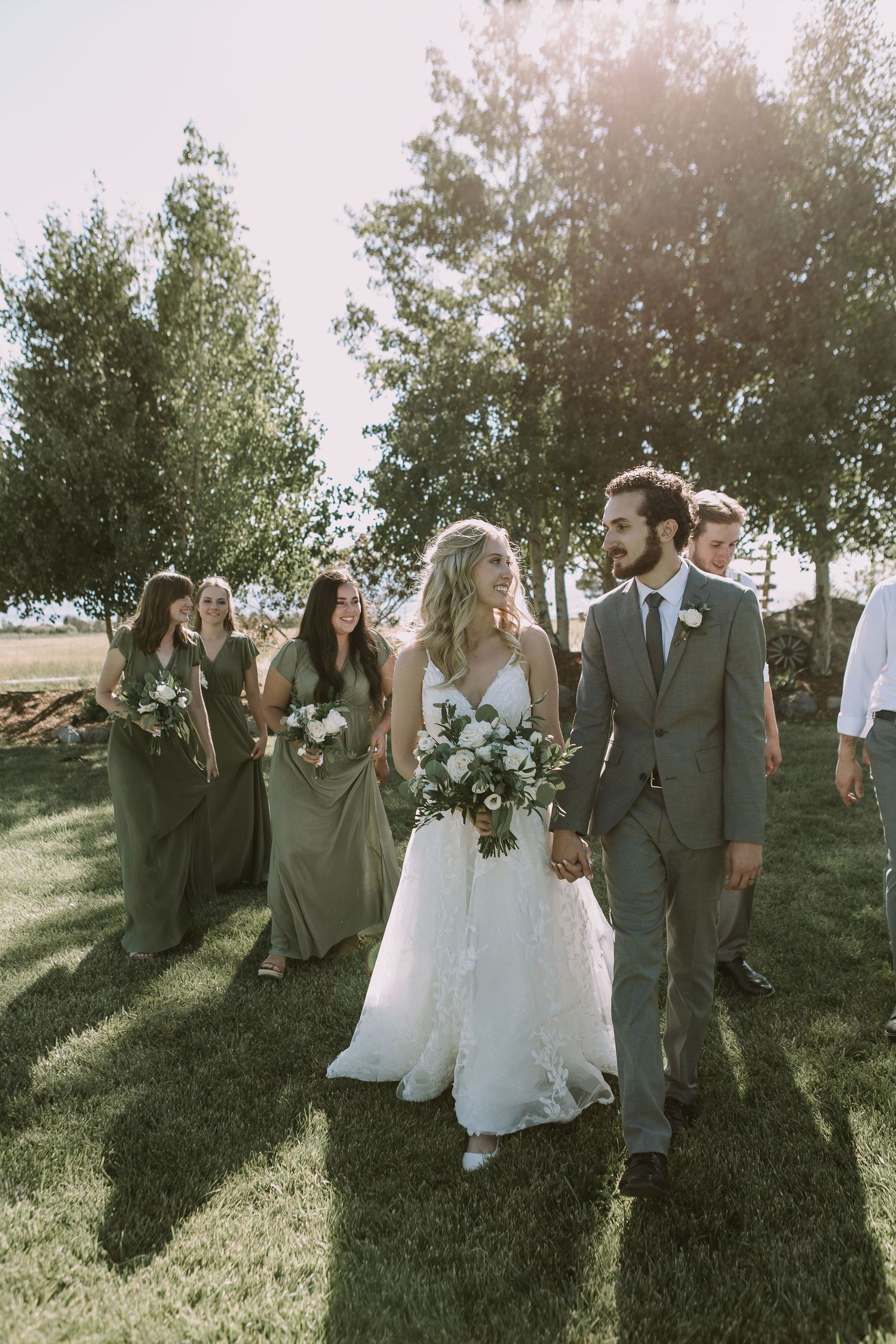 Wedding couple walks with bridal party through a sunlit outdoor garden setting.