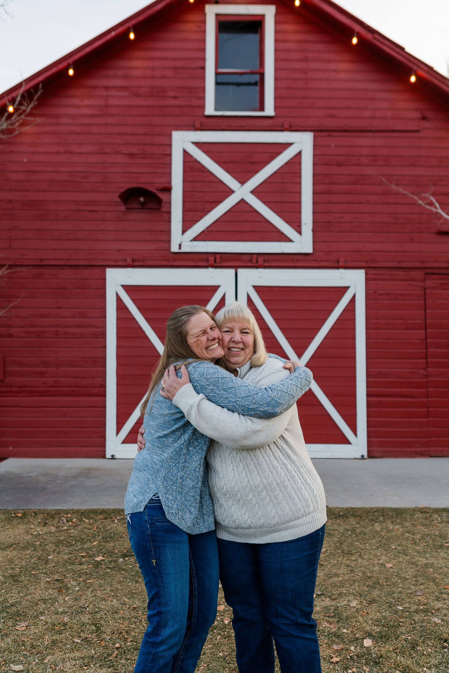 Two people sharing a warm embrace while standing in front of a bright red barn with white X details.
