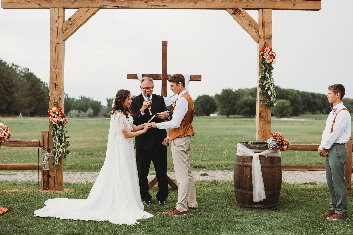 Rustic outdoor wedding ceremony under wooden arch with floral decorations.