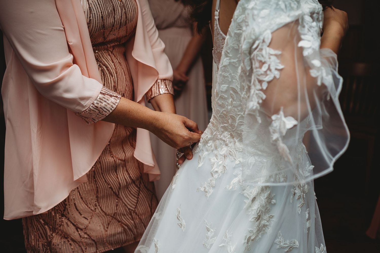Close-up detail of pink bridesmaid dress and white lace wedding gown being adjusted.