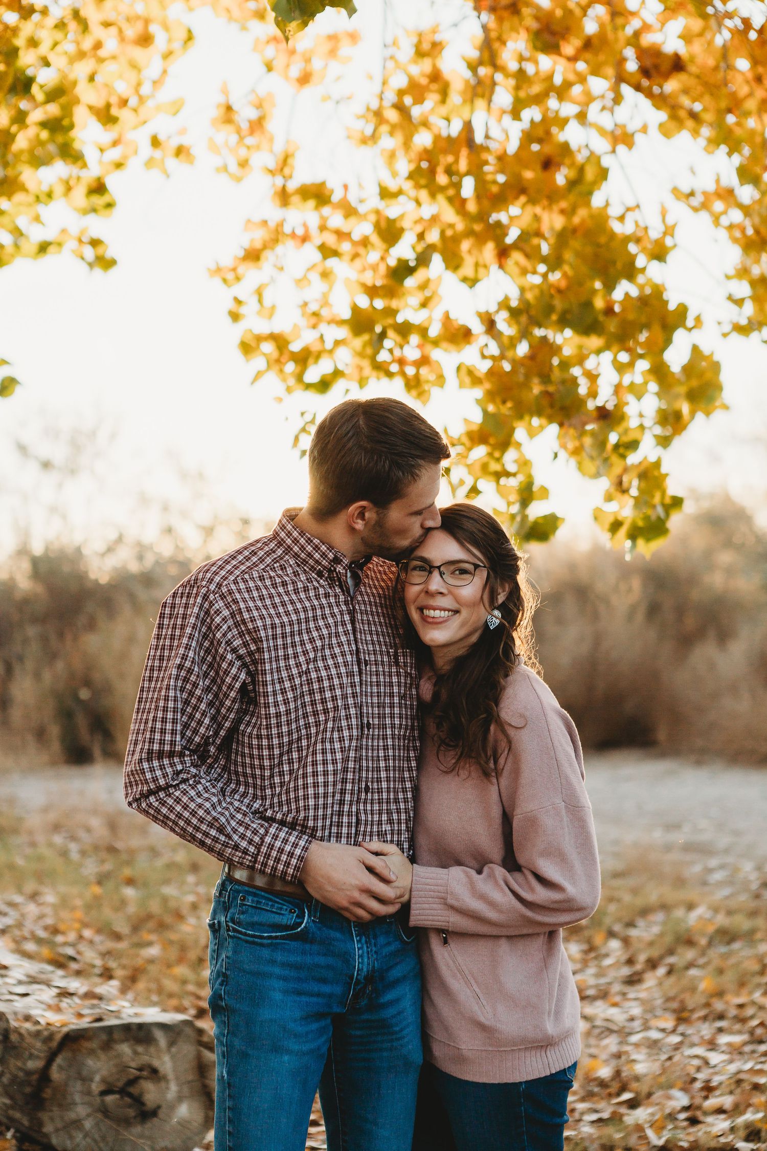Intimate moment shared between a couple in casual wear under golden autumn leaves.
